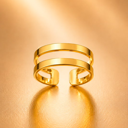 A gold open cuff ring with a minimalist, multi-band design, displayed on a warm, textured gold surface with a soft reflection.