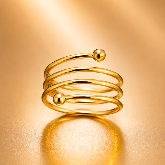 A gold-plated open wrap ring with two small spherical bead accents, displayed on a warm, reflective gold surface.
