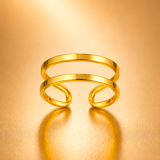 A gold open cuff ring with a modern, double-band design, displayed on a warm, reflective gold surface with a soft reflection.