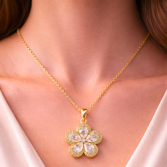 Gold necklace with a floral pendant worn by a person in a white garment.