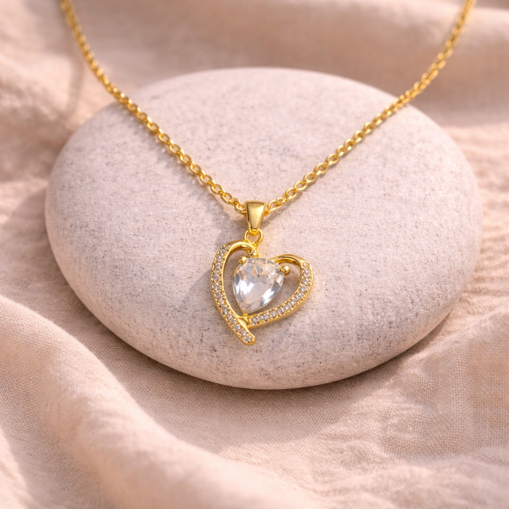 Gold heart-shaped necklace with a clear gemstone on a stone surface