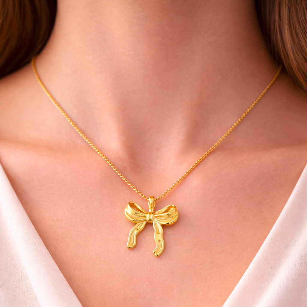 Gold necklace with a bow pendant worn by a person in a white top.