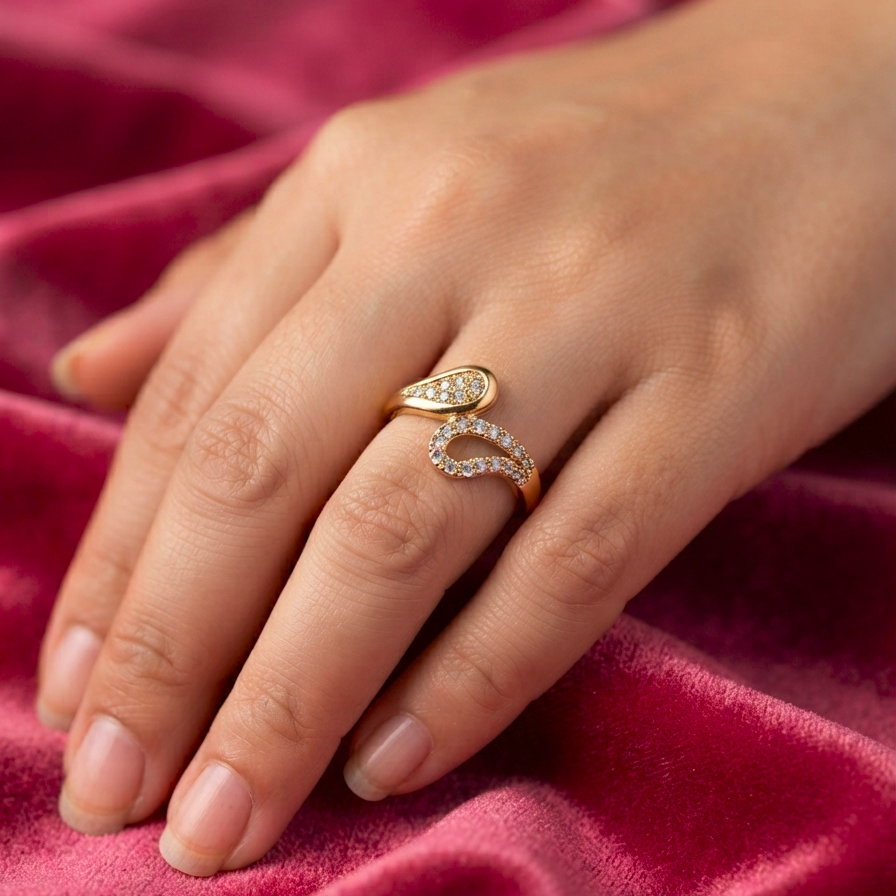 A close-up of a hand wearing a gold ring with two curved diamond-set bands, resting on a textured pink velvet fabric.