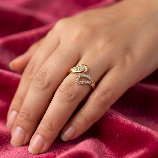 A close-up of a hand wearing a gold ring with two curved diamond-set bands, resting on a textured pink velvet fabric.