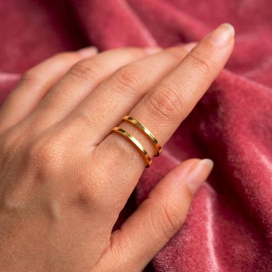 A close-up of a hand wearing two thin gold rings, resting on a textured, dusty rose velvet fabric.