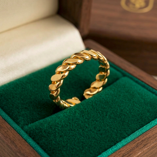 A gold-toned chunky curb-link ring displayed inside an open dark green velvet jewelry box with a wooden lid in the background.