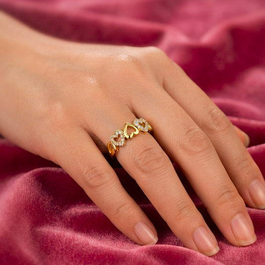 A close-up of a hand wearing a gold ring with small clear stones, resting on a draped dusty rose velvet fabric.