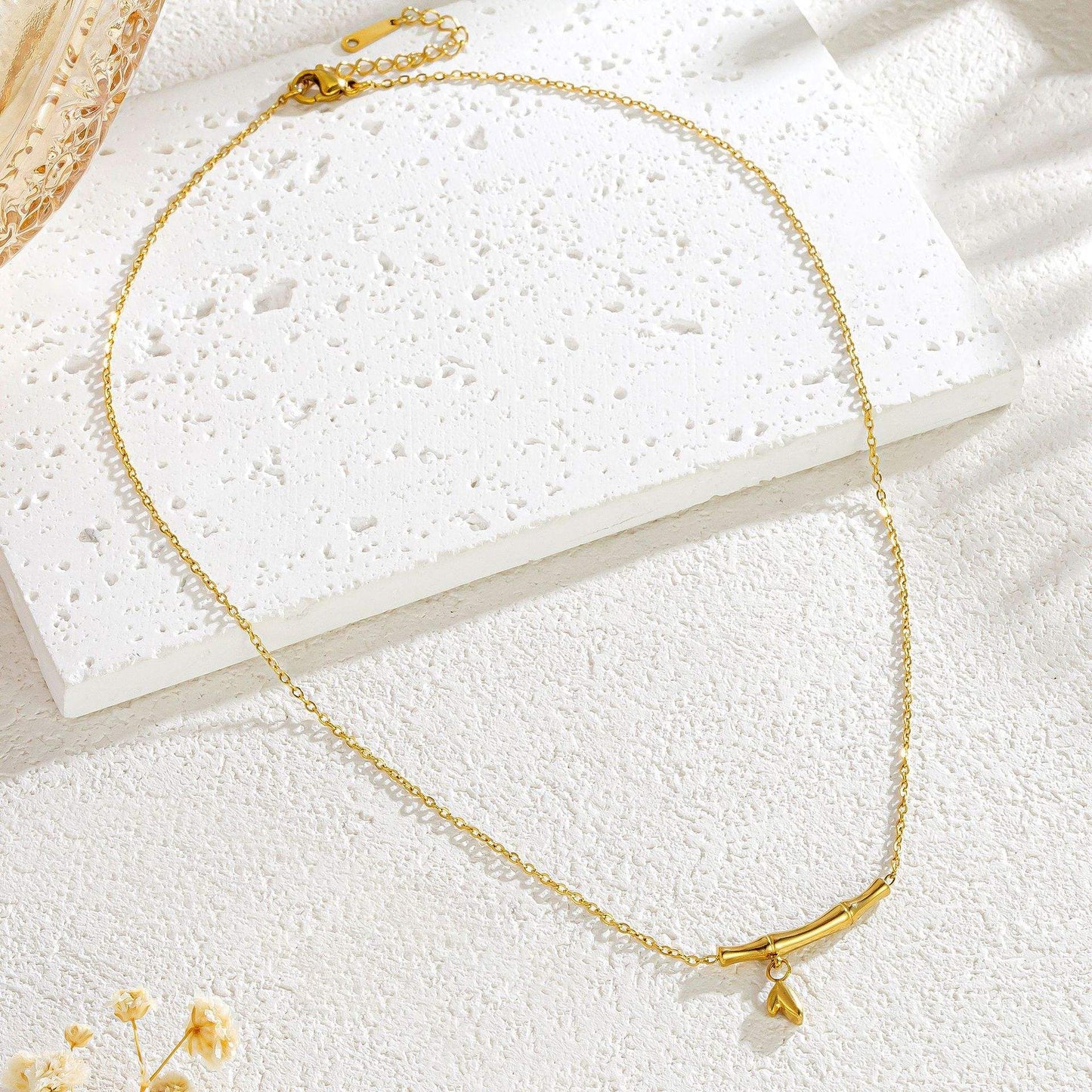 Gold necklace on a white textured surface with a small yellow flower.