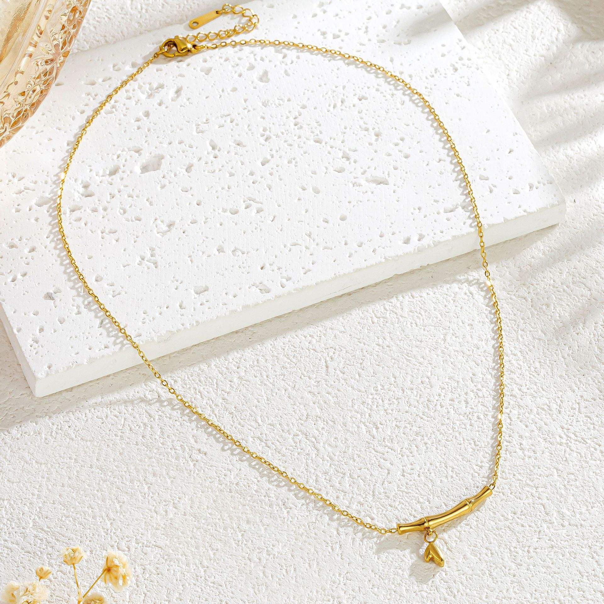 Gold necklace on a white textured surface with a small yellow flower.