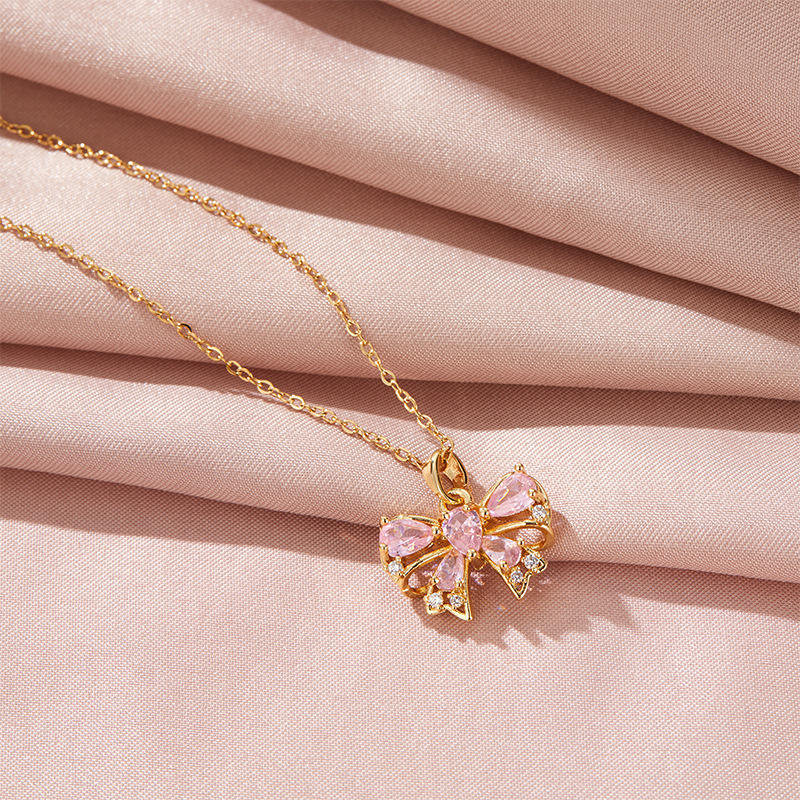 Gold butterfly necklace with pink gemstones on a pink fabric background