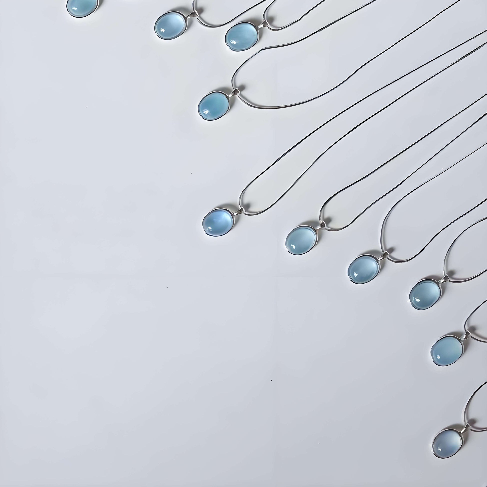 Multiple silver necklaces with blue teardrop pendants on a light gray background