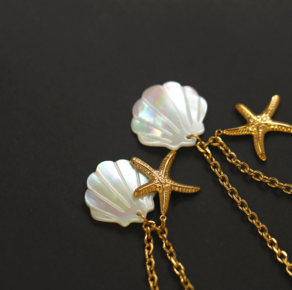 Gold chain earrings with starfish and shell designs on a black background