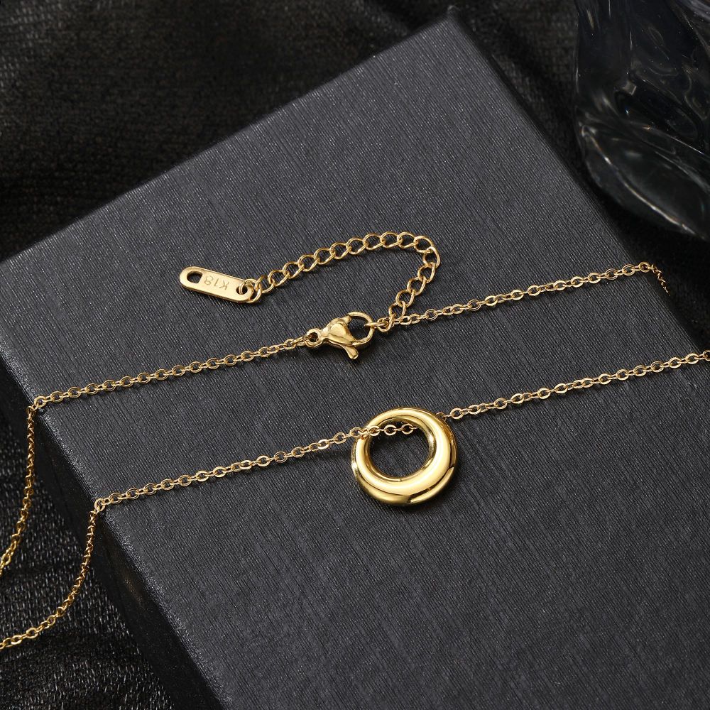 Gold necklace with a circular pendant on a black textured surface