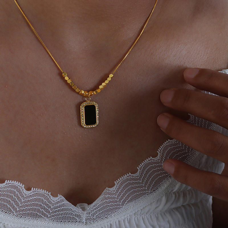 Gold necklace with a black pendant worn by a person, with a hand touching the neckline.