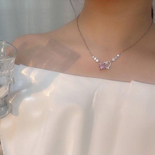 Necklace with a pink gemstone worn by a person, with a glass of water and white fabric in the background.