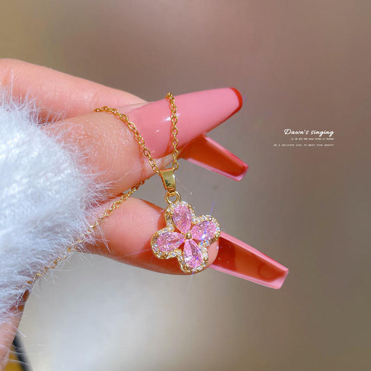 Gold necklace with a pink flower pendant held by a hand with red nail polish.