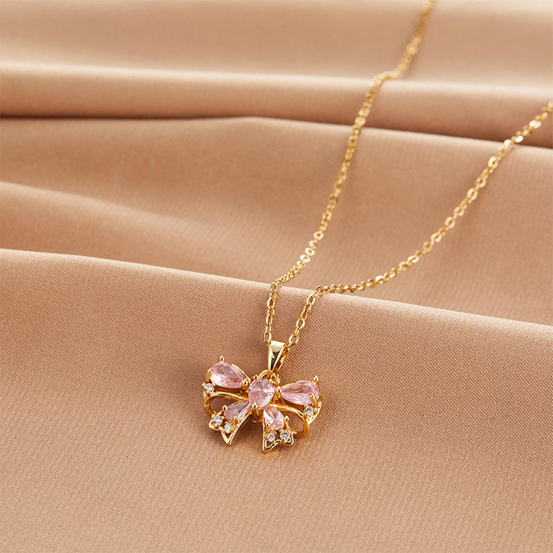 Gold necklace with a pink bow pendant on a beige fabric background