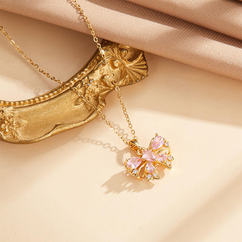 Gold necklace with a pink heart-shaped pendant on a beige fabric background