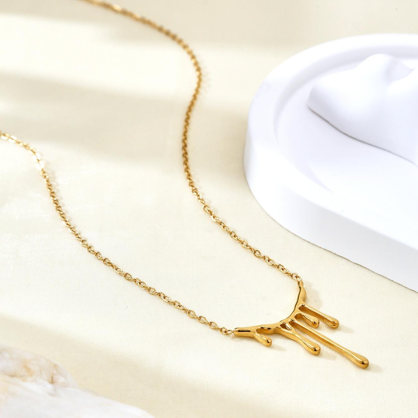 Gold necklace with a branch-like pendant on a light beige surface.