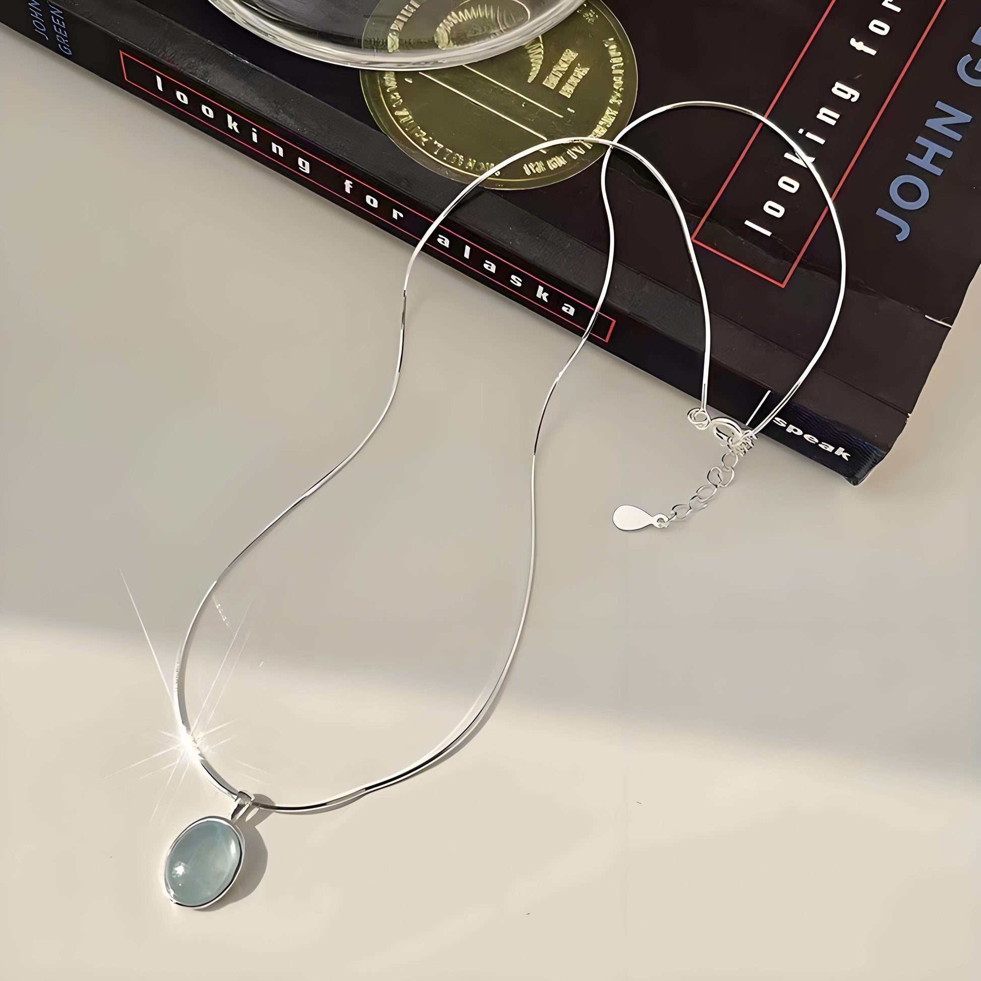 Silver necklace with a pendant on a white surface with a book in the background