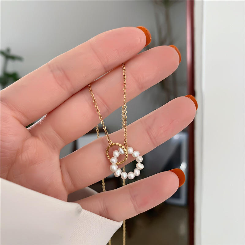 Hand holding a gold necklace with a heart-shaped pearl pendant against a blurred indoor background