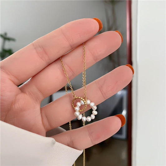 Hand holding a gold necklace with a heart-shaped pearl pendant against a blurred indoor background
