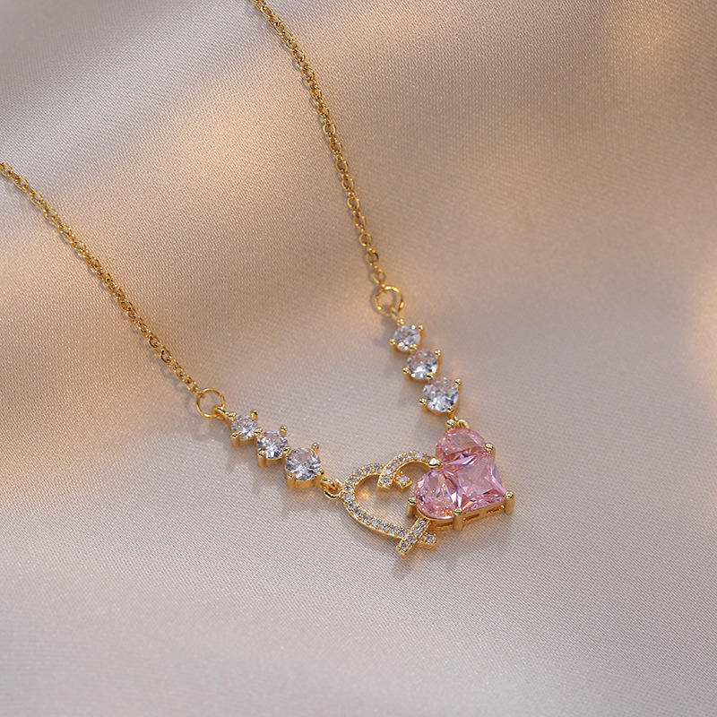 Gold necklace with a pink gemstone pendant on a beige fabric background