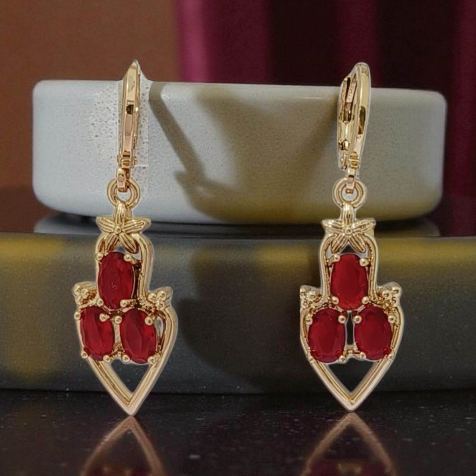 Gold earrings with red gemstones on a reflective surface