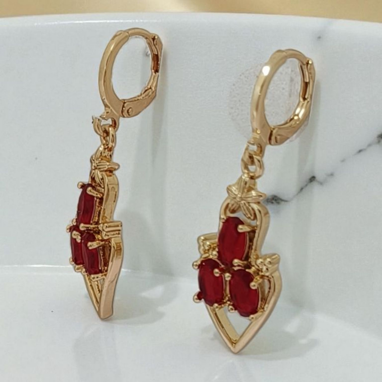 Gold earrings with red gemstones on a marble surface