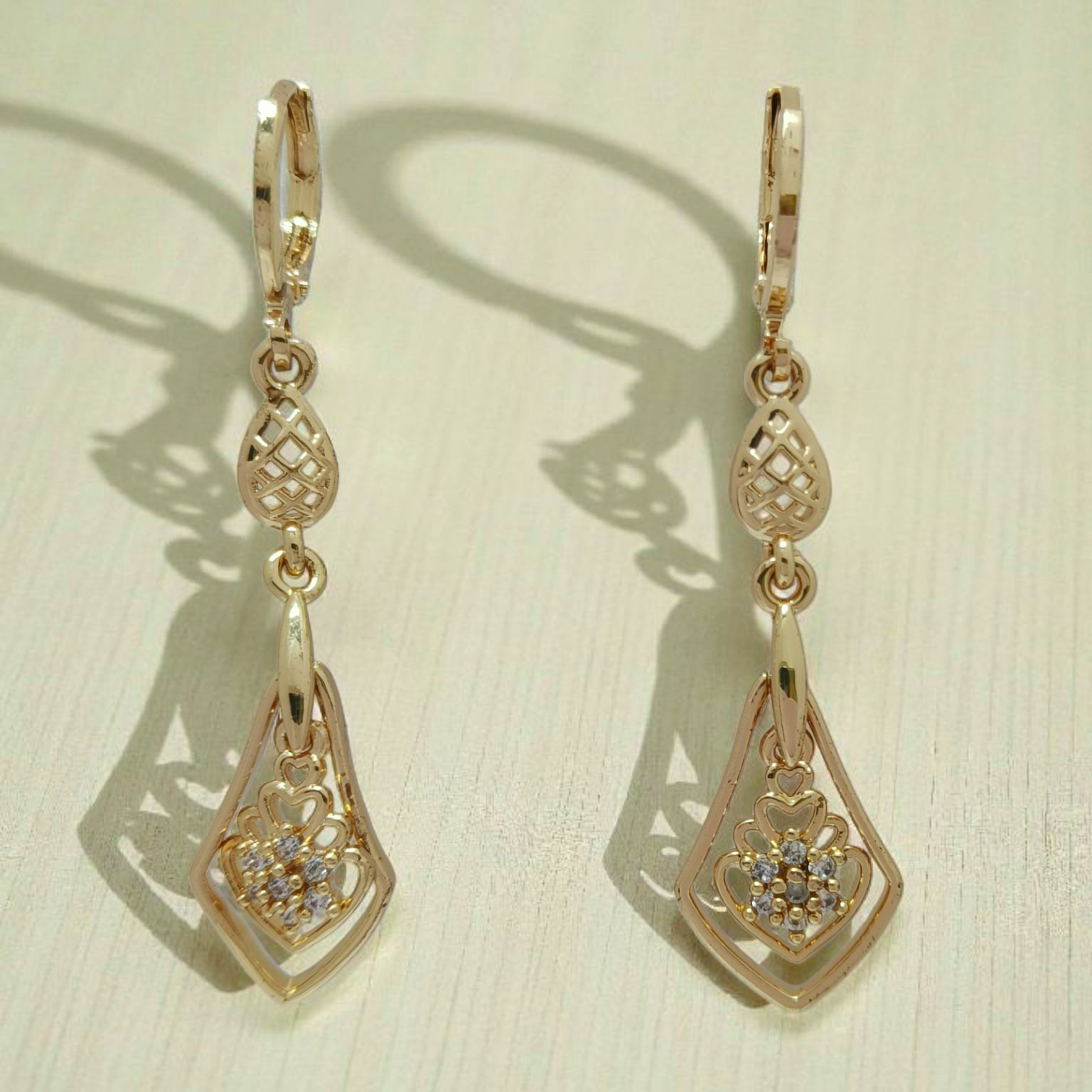 Pair of gold earrings with intricate designs on a beige background