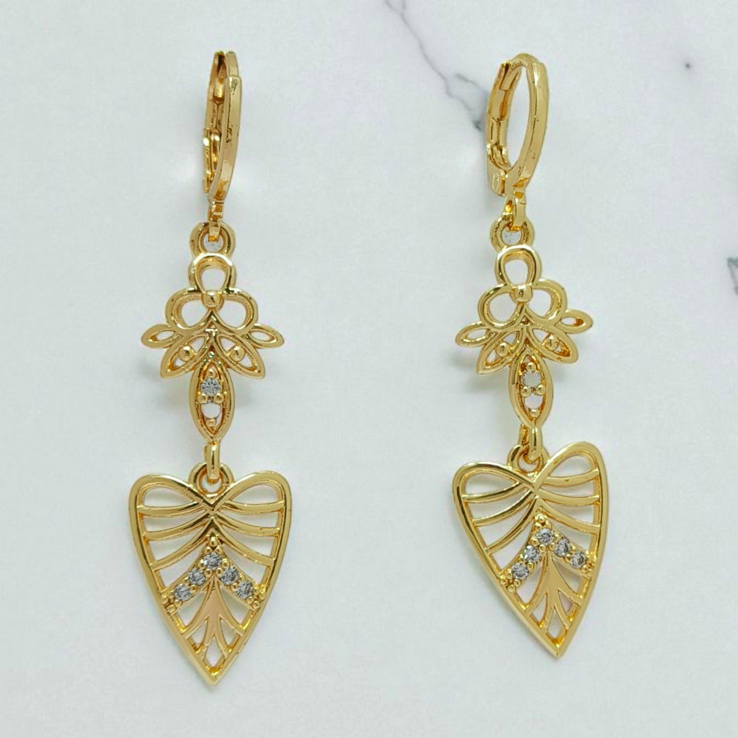 Gold earrings with floral and heart designs on a light background