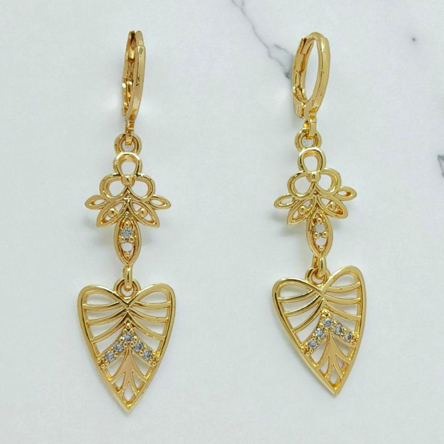 Gold earrings with floral and heart designs on a light background