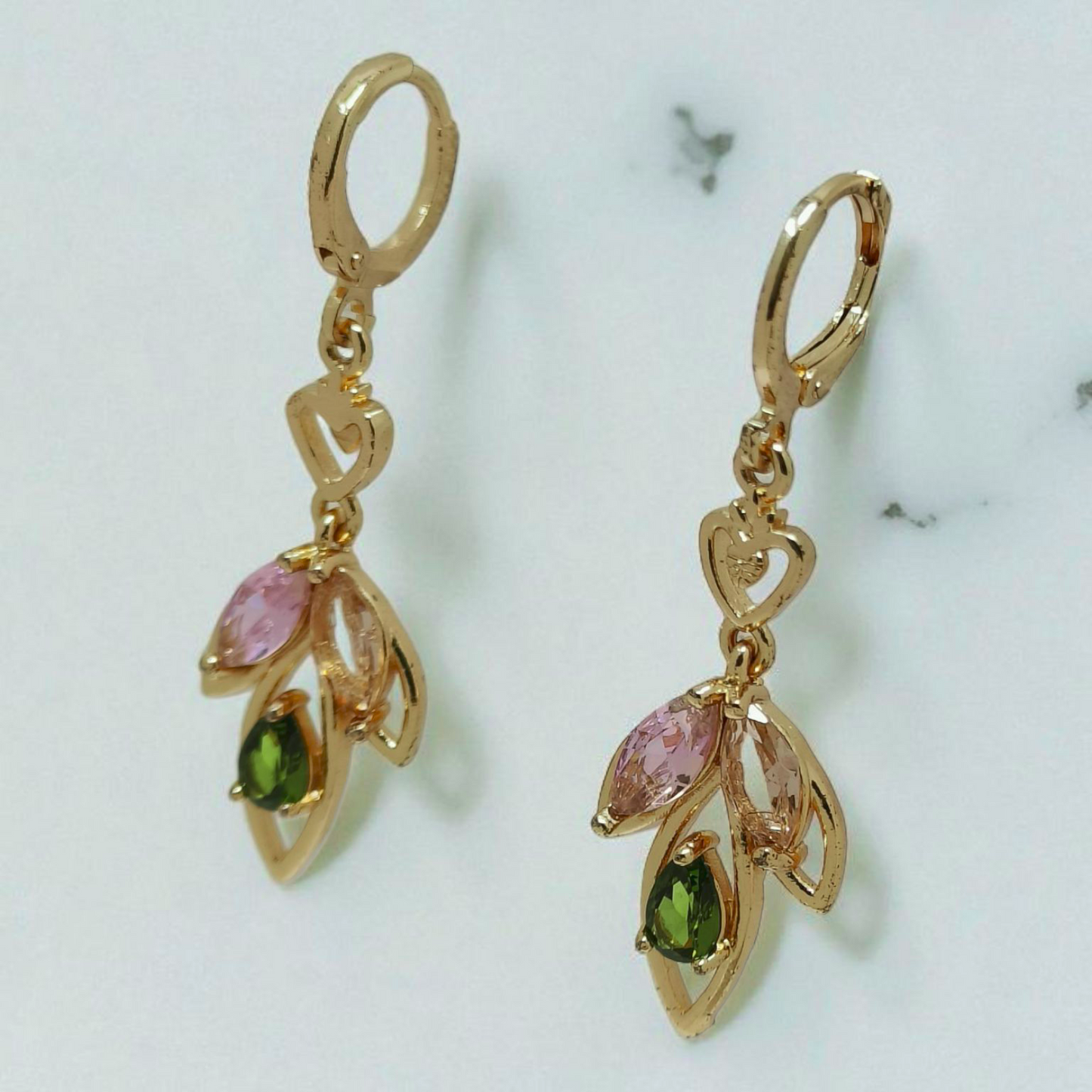 Gold earrings with pink and green gemstones on a marble surface