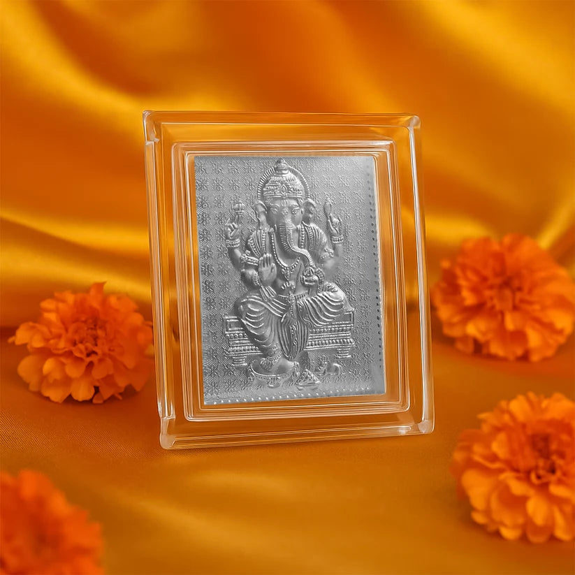 Silver deity panel in a clear frame on an orange fabric background with marigold flowers.