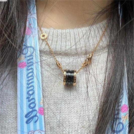 Gold necklace with a black pendant worn by a person with a colorful scarf.