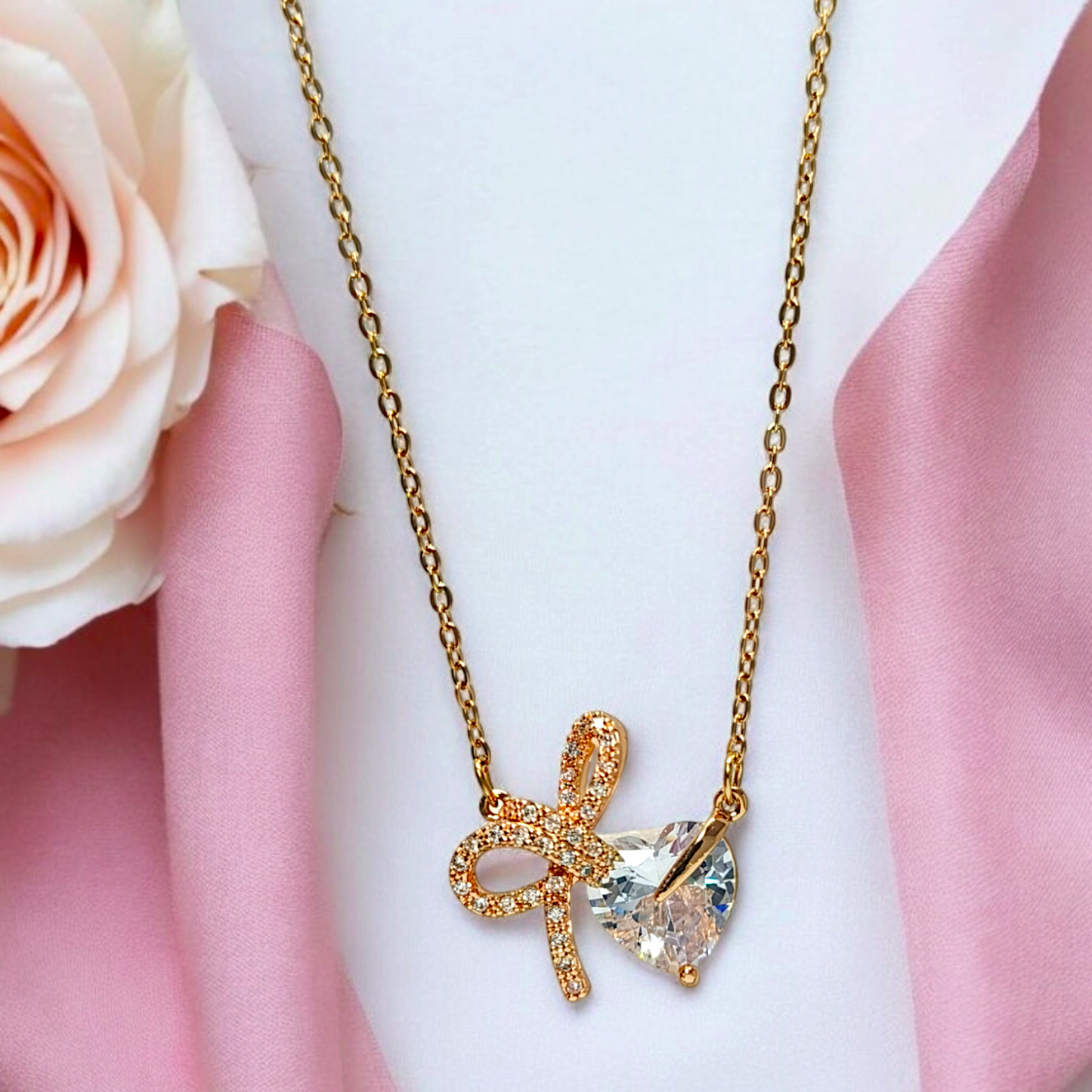 Gold necklace with a bow and heart pendant on a pink fabric background