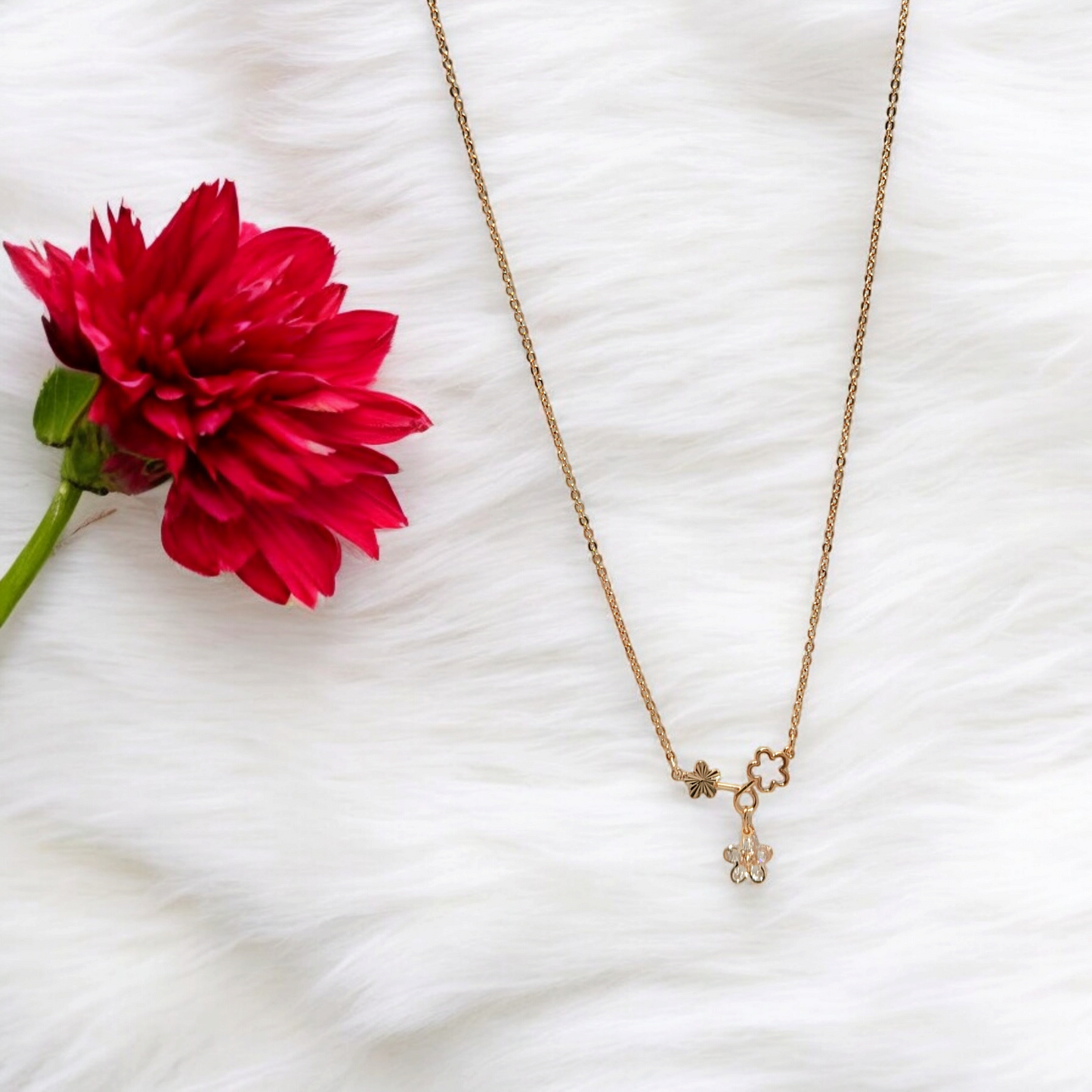 Gold necklace with a red flower on a white textured surface
