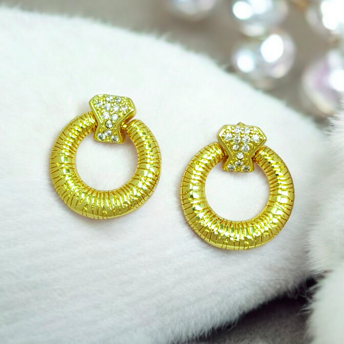 Gold hoop earrings on a white fur surface with blurred background