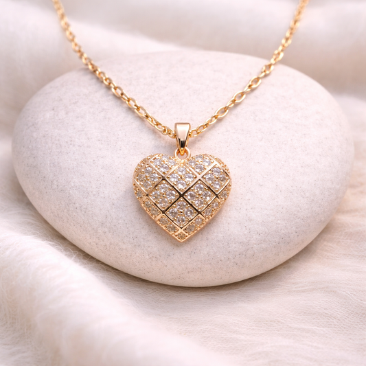 Gold heart-shaped necklace with diamond-like stones on a white stone surface