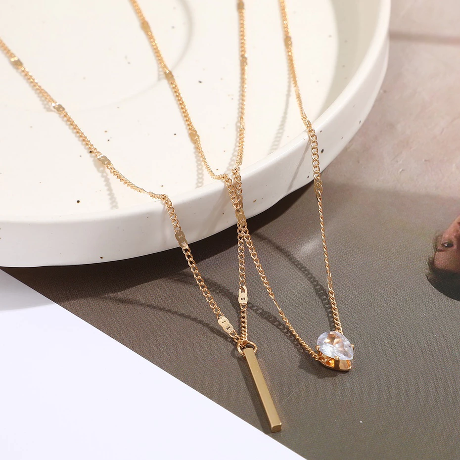 Two gold necklaces with pendants on a reflective surface.
