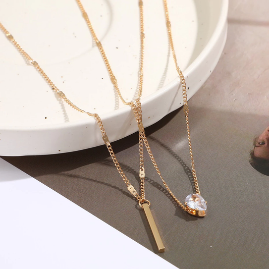 Two gold necklaces with pendants on a reflective surface.
