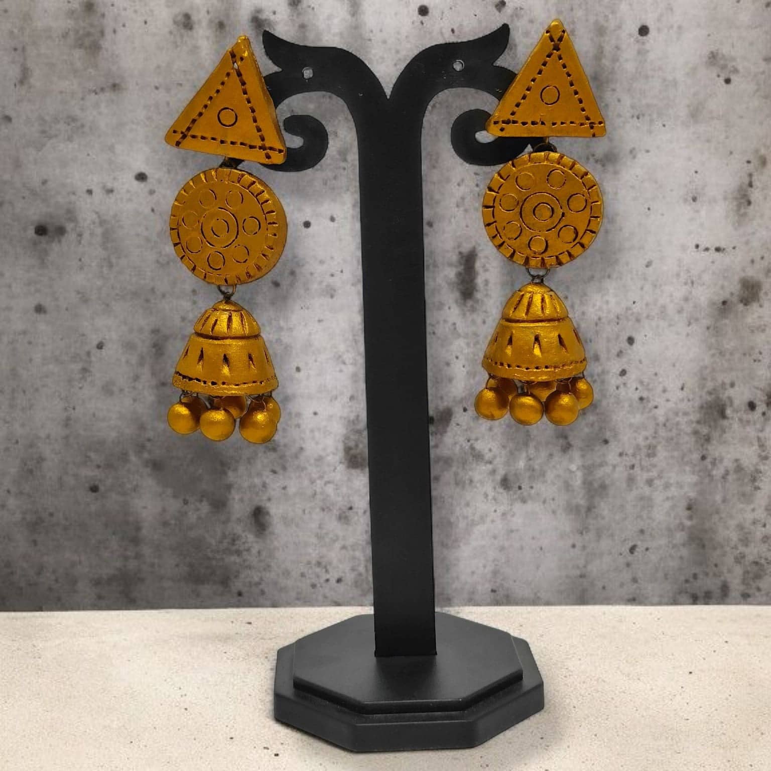 Handmade Terracotta Jhumka Earrings in yellow with intricate patterns displayed on black stand