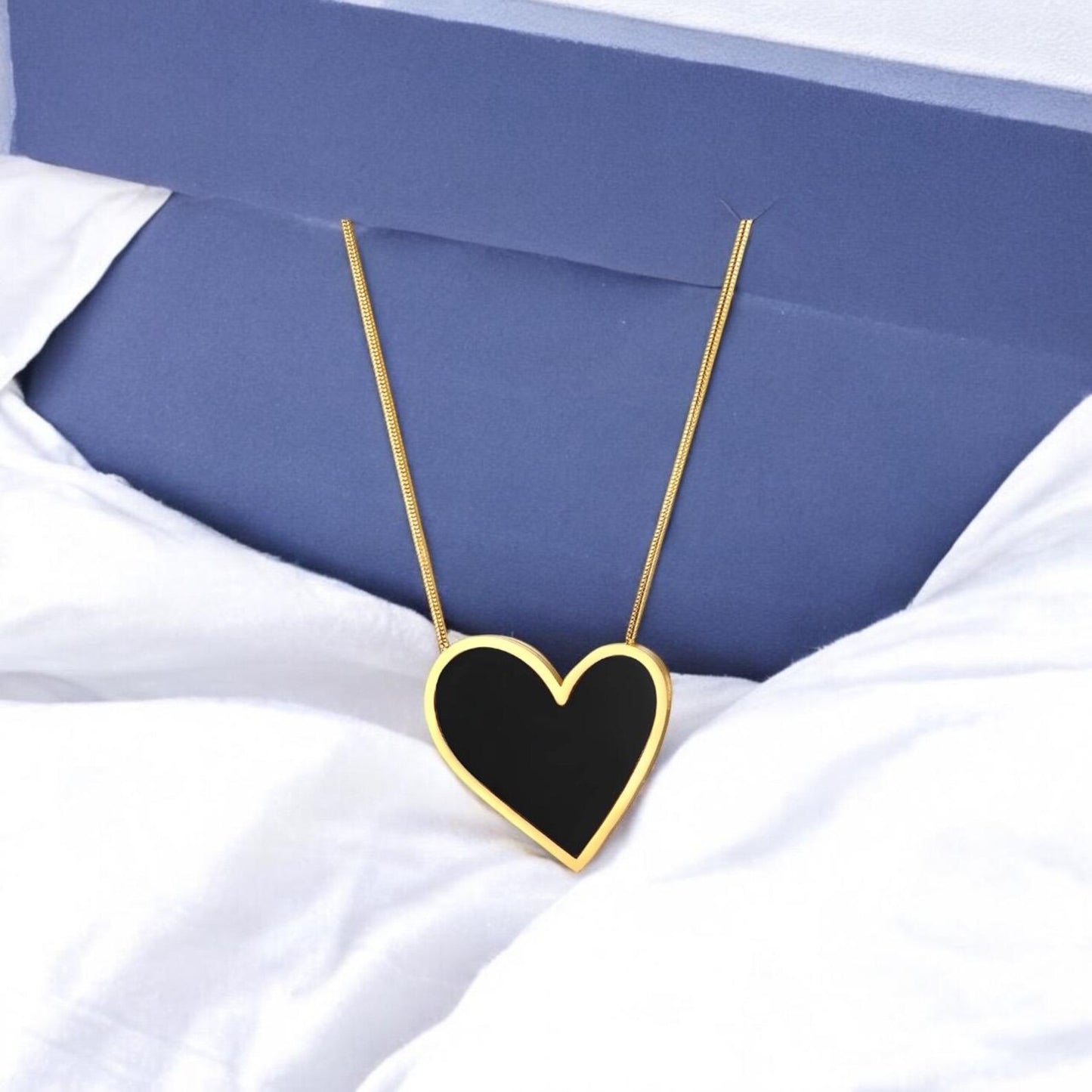 Heart-shaped necklace with black heart pendant on a white fabric background