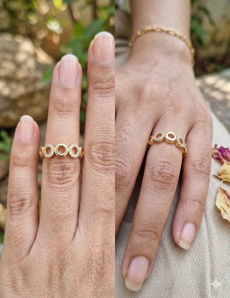 A close-up split view of a person's hand wearing a delicate gold ring with three interlocking circular motifs. The background is softly blurred with natural outdoor light and neutral fabric visible.
