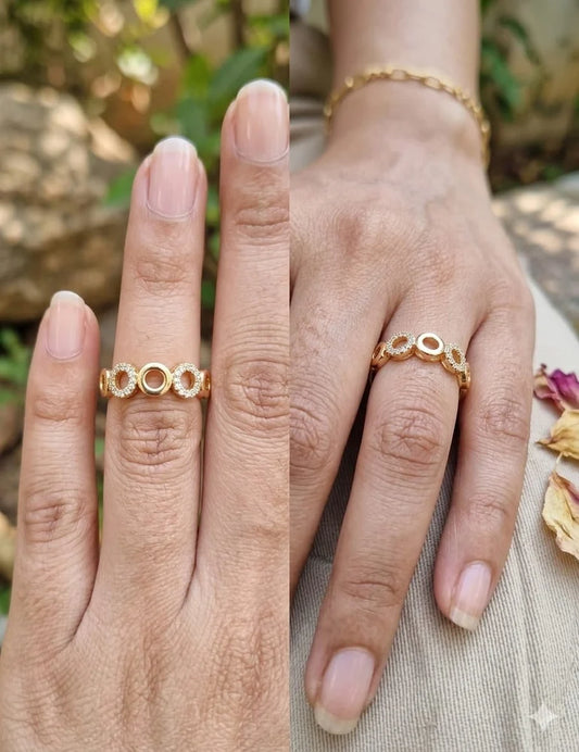 A close-up split view of a person's hand wearing a delicate gold ring with three interlocking circular motifs. The background is softly blurred with natural outdoor light and neutral fabric visible.